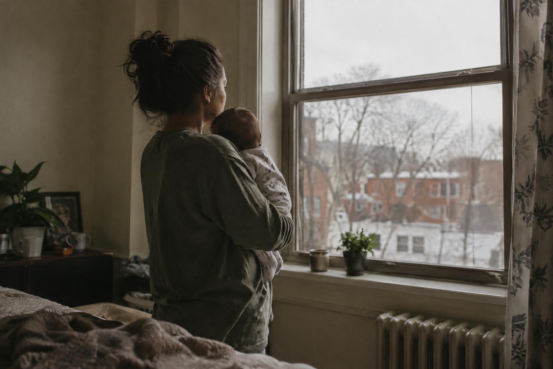 A mother holding her baby beside an open window