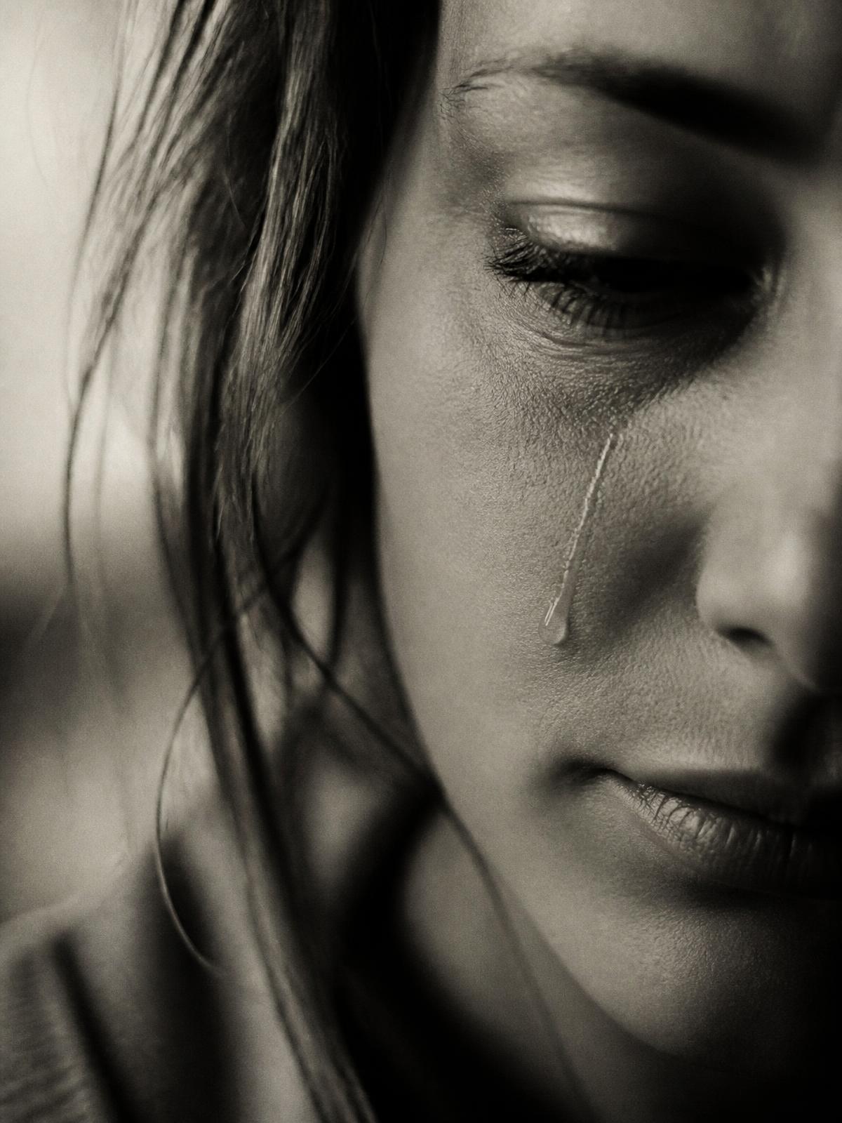 A close-up portrait of a single tear tracing a woman's cheek